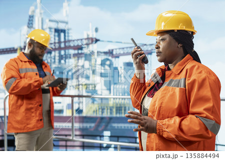 Drilling rig team leader uses two way radio to establish communication with logistics personnel. Offshore platform expert speaks in walkie talkie providing audio clarity in noisy environment 135884494