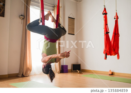 Woman practicing aerial yoga inversion in hammock Woman practicing aerial yoga inversion in hammock 135884859