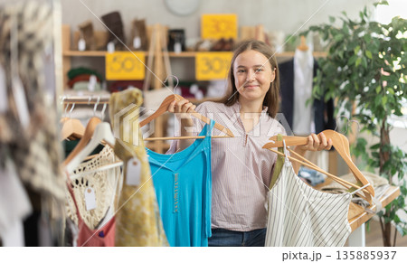 Positive teenage girl choosing something for summer in clothing store 135885937