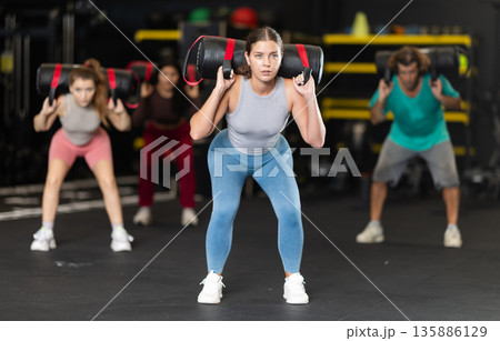 Determined young woman performing sandbag squats Determined young woman performing sandbag squats 135886129
