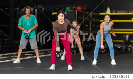 Sportive Latina girl lifting heavy kettlebell in sports hall Sportive Latina girl lifting heavy kettlebell in sports hall 135886131
