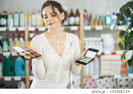 Woman purchases household chemicals in store and chooses eye shadow pallet 135886134