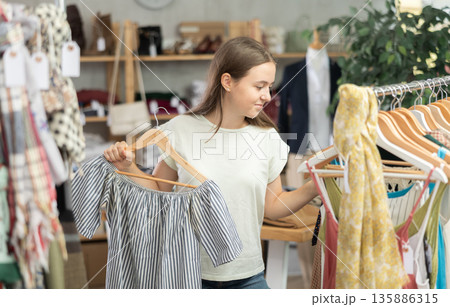 Positive teenage girl choosing something for summer in clothing store 135886315