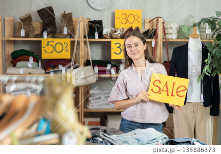 Young teenage girl holding a sign saying Sale in the interior of fashion store 135886373