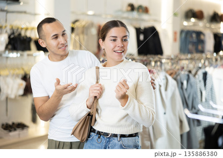 Young couple watching excitedly large stock of clothes in clothing store Young couple watching excitedly large stock of clothes in clothing store 135886380