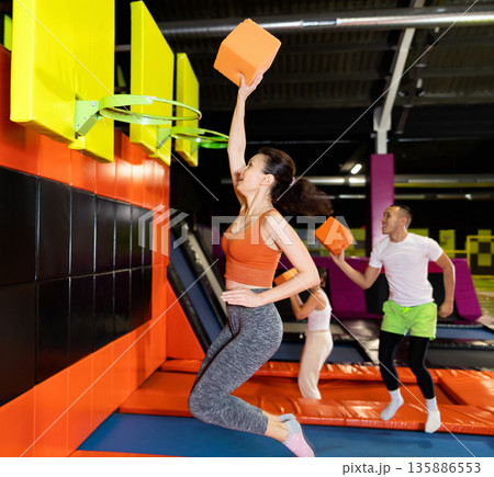 Athletic people throw ball into basketball basket while jumping on trampolines at an entertainment center Athletic people throw ball into basketball basket while jumping on trampolines at an entertainment center 135886553