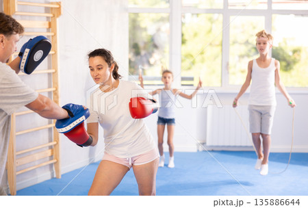 Woman in boxing gloves punching pads in hands of husband during family traning Woman in boxing gloves punching pads in hands of husband during family traning 135886644