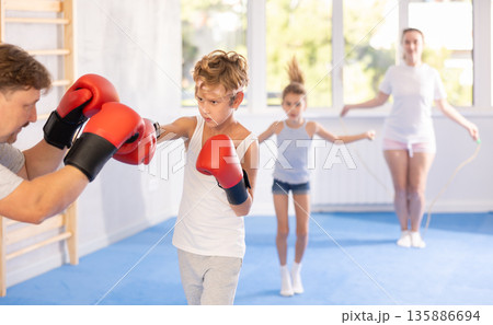 Tweenager in boxing gloves sparring with father during family training Tweenager in boxing gloves sparring with father during family training 135886694