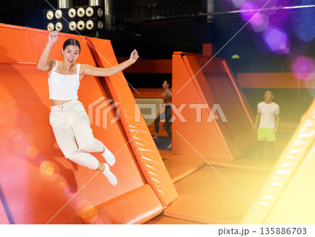 Portrait of sporty girl jumping on trampolines in her free time in gaming club Portrait of sporty girl jumping on trampolines in her free time in gaming club 135886703