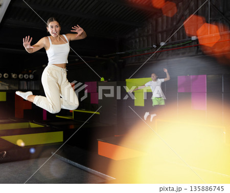 Happy girl bouncing on trampoline in indoor amusement park Happy girl bouncing on trampoline in indoor amusement park 135886745