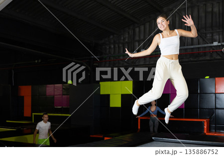 Happy girl bouncing on trampoline in indoor amusement park Happy girl bouncing on trampoline in indoor amusement park 135886752