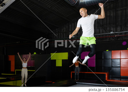 Cheerful young man jumping in modern indoor trampoline park Cheerful young man jumping in modern indoor trampoline park 135886754
