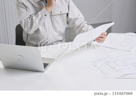 図面を持ってデスクで考える作業員　顔無し 135887066