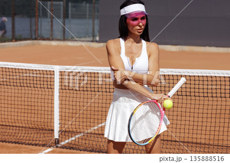 Female tennis athlete poses with racket and ball by the net on a clay court. Ideal for sports club website banner or social advertising. 135888516