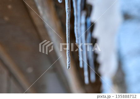 Close-up of frozen icicles dripping from a wooden roof against a blurred winter sky Close-up of frozen icicles dripping from a wooden roof against a blurred winter sky 135888712