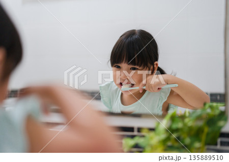 girl child brushing teeth at reflection in mirror in bathroom girl child brushing teeth at reflection in mirror in bathroom 135889510