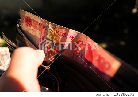 Chinese Yuan Cash Payment, A hand pulls a red 100 Yuan banknote from a leather wallet Chinese Yuan Cash Payment, A hand pulls a red 100 Yuan banknote from a leather wallet 135890273