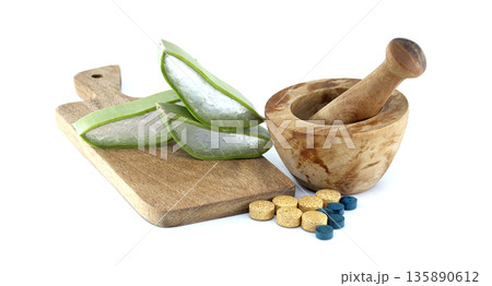 Aloe vera slices and pills next to a wooden mortar and pestle on a cutting board 135890612