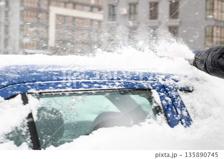 Clearing snow for safe visibility, Person removes thick snow from vehicle in winter conditions 135890745