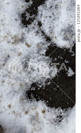 Close-up of snow-covered ground with dark patches. 135891064