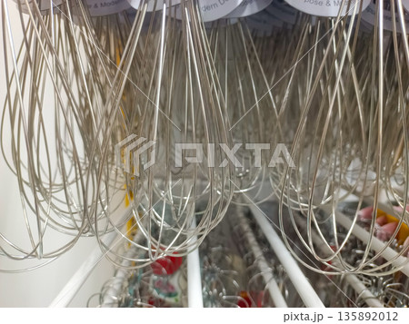Close Up Many Stainless Steel Wire Whisks Hanging on Display Rack in Kitchenware Store 135892012
