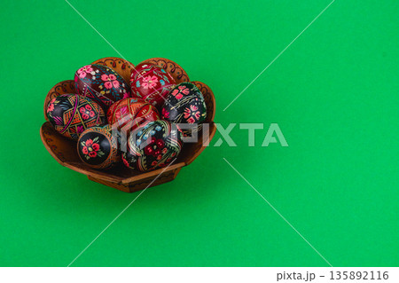 Decorative eggs in a wooden bowl on a green background 135892116