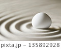White egg on smooth surface creates gentle ripples in sand 135892928