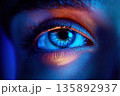 Close-up of a striking blue eye illuminated by colorful lighting effects 135892937