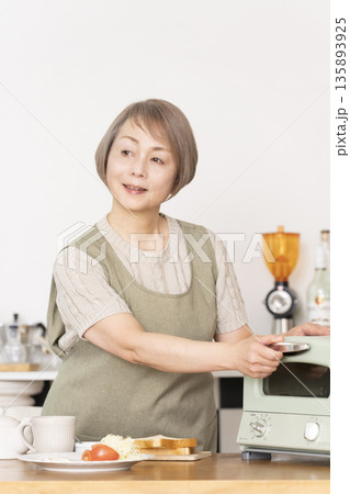 キッチンでトーストを焼いて朝食を食べるシニア女性 135893925