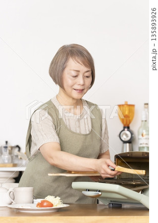 キッチンでトーストを焼いて朝食を食べるシニア女性 135893926