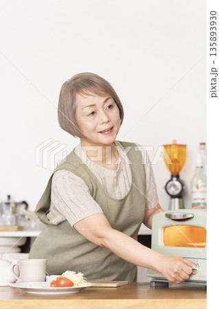 キッチンでトーストを焼いて朝食を食べるシニア女性 キッチンでトーストを焼いて朝食を食べるシニア女性 135893930