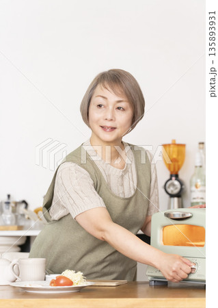 キッチンでトーストを焼いて朝食を食べるシニア女性 135893931