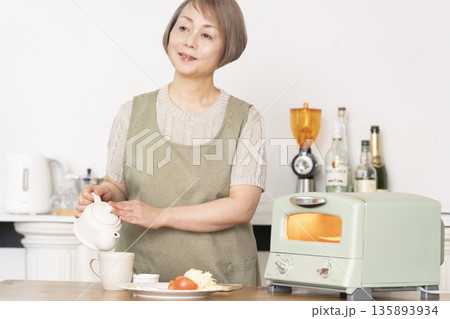 キッチンでトーストを焼いて朝食を食べるシニア女性 キッチンでトーストを焼いて朝食を食べるシニア女性 135893934