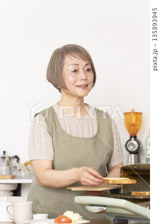 キッチンでトーストを焼いて朝食を食べるシニア女性 135893945