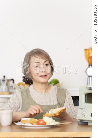 キッチンでトーストを焼いて朝食を食べるシニア女性 キッチンでトーストを焼いて朝食を食べるシニア女性 135893955