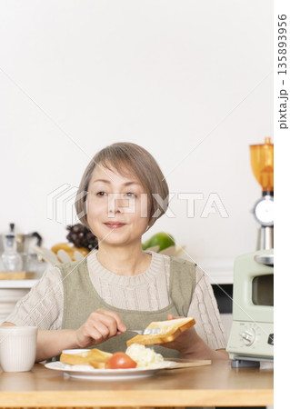 キッチンでトーストを焼いて朝食を食べるシニア女性 キッチンでトーストを焼いて朝食を食べるシニア女性 135893956