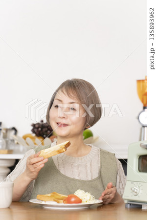 キッチンでトーストを焼いて朝食を食べるシニア女性 135893962