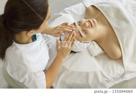 Head massage, facial spa treatment, anti age procedure for clients skin by cosmetologist, top view 135894069