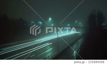 A lonely car moves across the overpass its headlights casting a long trail of light as it disappears into the darkness 135894398