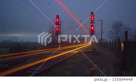 The humble train crossing in the rural countryside becomes a picturesque moment with light trails from passing cars 135894449