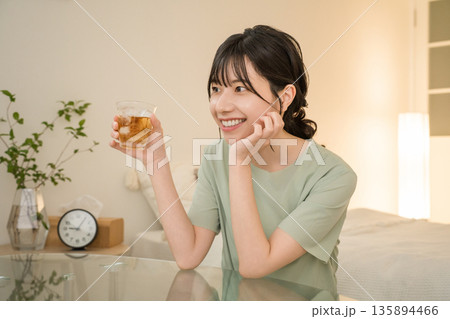 自宅の寝室で晩酌をする若いアジア人女性（家飲み,ほろ酔い,宅飲み,酒飲み） 135894466