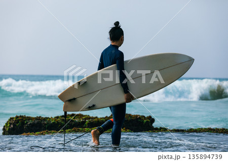 Woman surfer with surfboard going to surf the big waves Woman surfer with surfboard going to surf the big waves 135894739