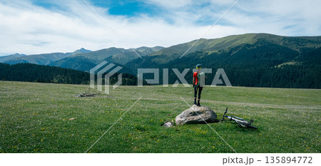 Aerial view of woman cyclist with mountain bike on flowering grassland mountain Aerial view of woman cyclist with mountain bike on flowering grassland mountain 135894772