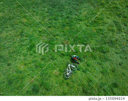 Aerial view of woman riding mountain bike on flowering grassland mountain trail 135894814