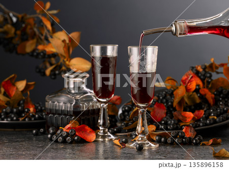 Black chokeberry liqueur and fresh berries on a black stone table. Black chokeberry liqueur and fresh berries on a black stone table. 135896158