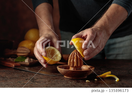 Chef squeezes juice from fresh lemons using an old wooden juicer. Chef squeezes juice from fresh lemons using an old wooden juicer. 135896173