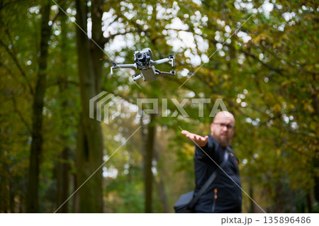 In a lush forest during autumn, a man extends his hand as a drone takes flight, exploring the rich colors of trees around him. Technology meets nature in harmony. In a lush forest during autumn, a man extends his hand as a drone takes flight, exploring the rich colors of trees around him. Technology meets nature in harmony. 135896486