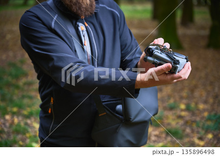 Individual carefully holds a compact drone, getting ready to launch it in a serene outdoor space filled with greenery. Focus is on the exciting activity ahead. 135896498