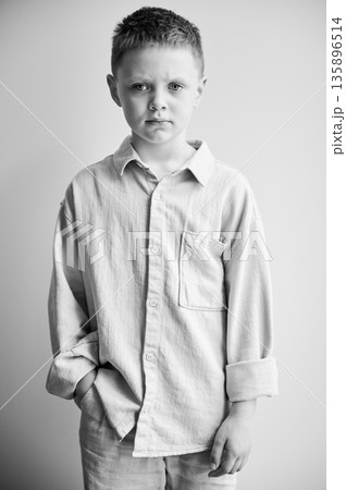 Portrait of young sad boy keeping hand in pocket, looking to the camera. Serious kid in casual clothes posing on white background. Black and white image. 135896514