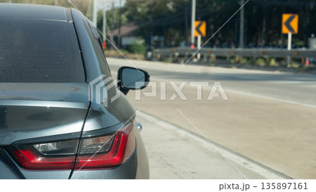 Rear side view of grey car on the concrete road. Closed on taillight of car. Driving alone on the road with traffic sign and guardrail. Clear roads and traffic. Rear side view of grey car on the concrete road. Closed on taillight of car. Driving alone on the road with traffic sign and guardrail. Clear roads and traffic. 135897161